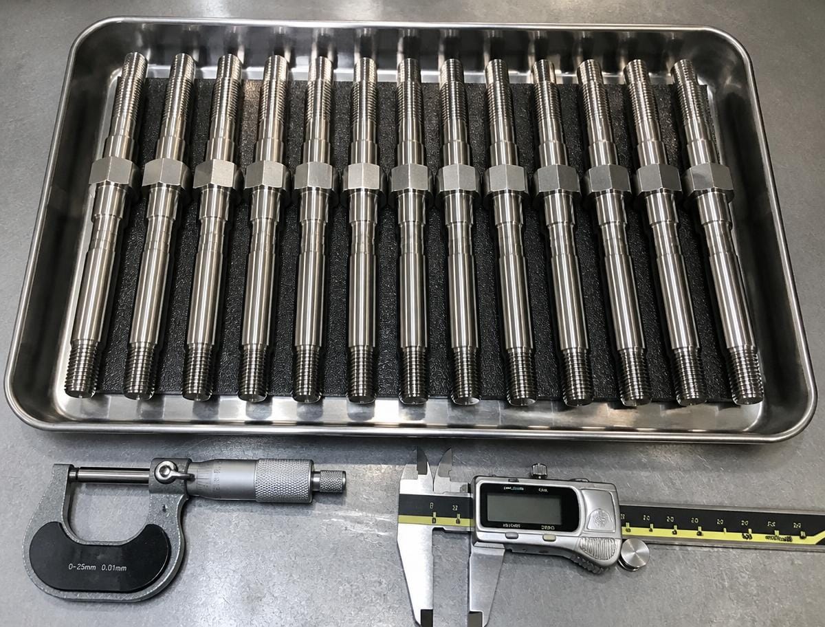 Precision machined superalloy studs in an inspection tray with micrometer and calipers